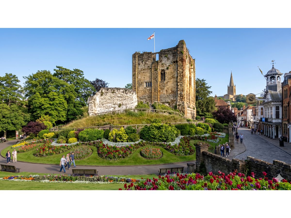 Guildford Castle keep and ornamental gardens in summer, with the High Street and Guildhall clock tower visible in the background, Surrey